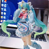 A PVC collectible figurine of Hatsune Miku with light blue hair and outfit standing in front of a laptop.