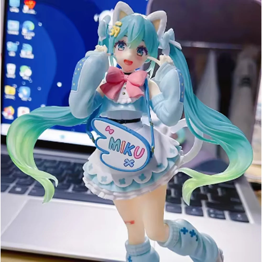 A PVC collectible figurine of Hatsune Miku with light blue hair and outfit standing in front of a laptop.