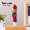 A tall glass bottle filled with pink and purple crystals topped by a red stone, representing Sagittarius zodiac sign.