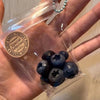 A clear plastic bag contains several dark blue blueberries, packaged for sale.
