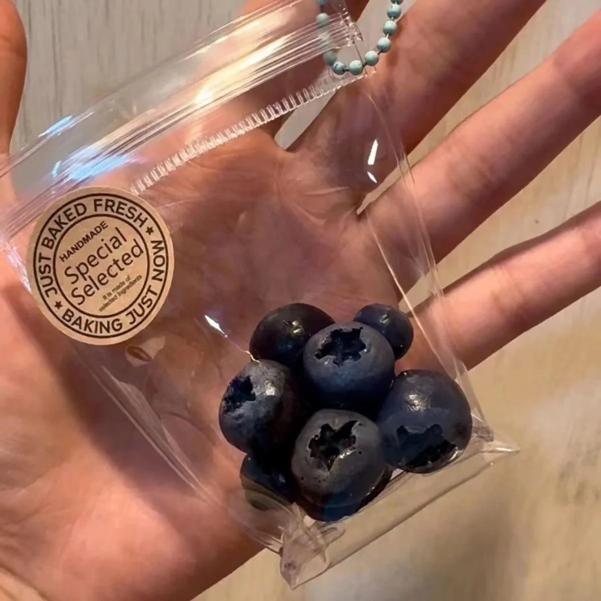 A clear plastic bag contains several dark blue blueberries, packaged for sale.