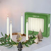 A set of ivory white drip-free stick candles displayed in front of a green box.