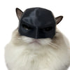 A black bat cat mask is placed on the face of a white, fluffy cat.