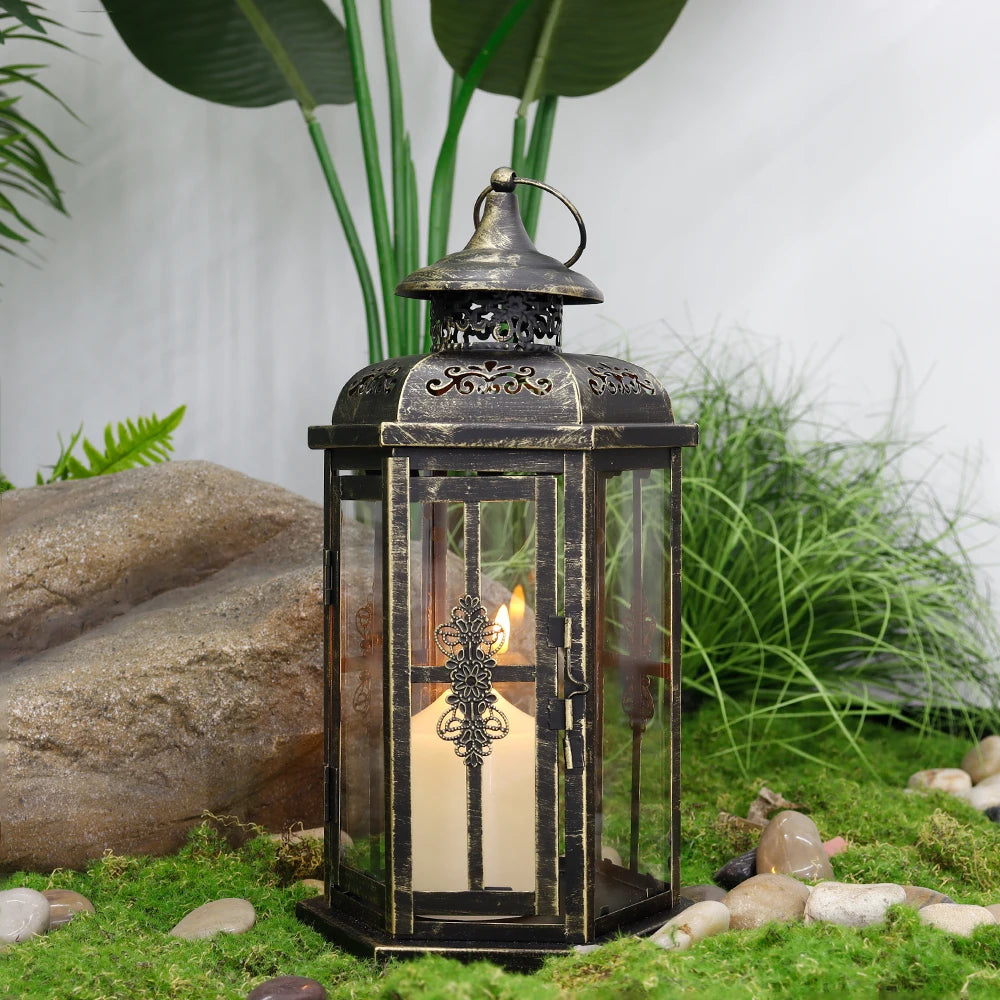 A vintage Nordic iron candle lantern with glass panes sits on mossy ground next to a large rock and green foliage.