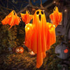 An orange LED ghost hanging decoration light with glowing eyes is displayed in an outdoor Halloween setting.