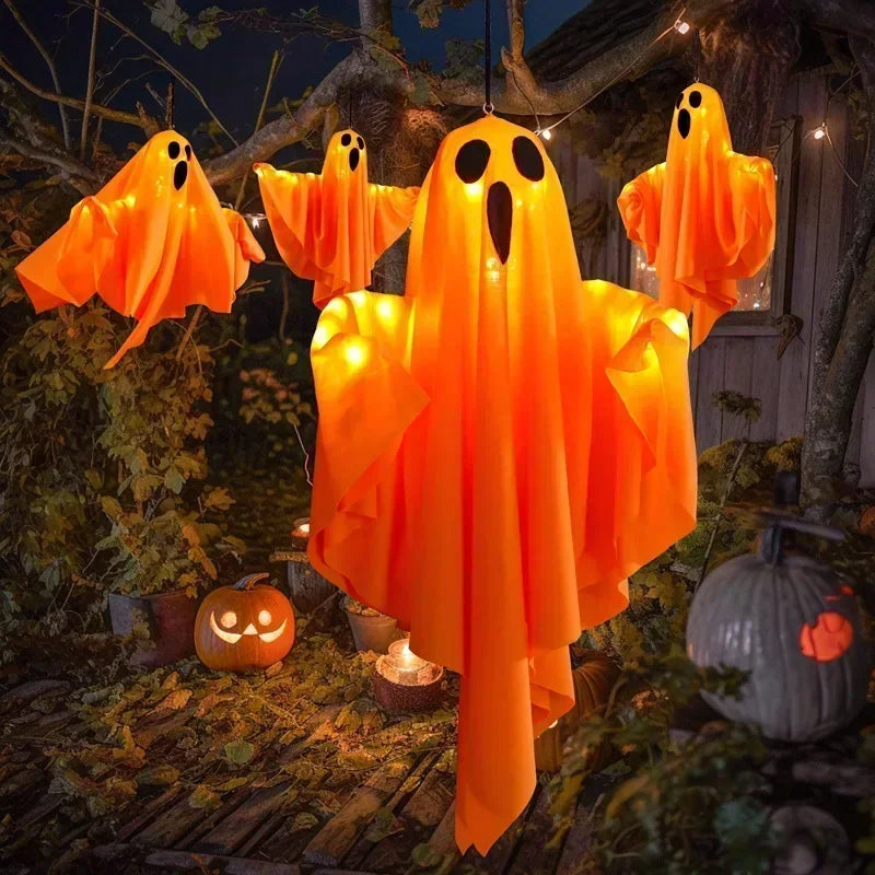 An orange LED ghost hanging decoration light with glowing eyes is displayed in an outdoor Halloween setting.