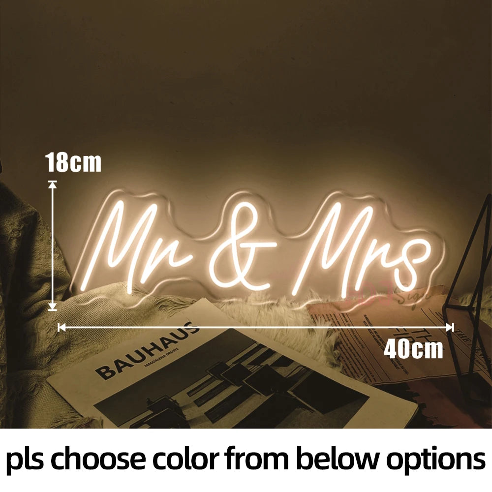 A glowing neon sign spelling out Mr & Mrs on a surface next to a Bauhaus print.