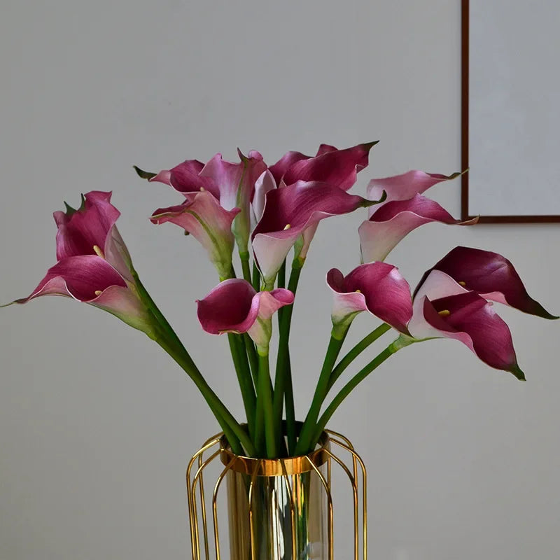 A bouquet of purple and pink artificial calla lily stems in a gold vase.