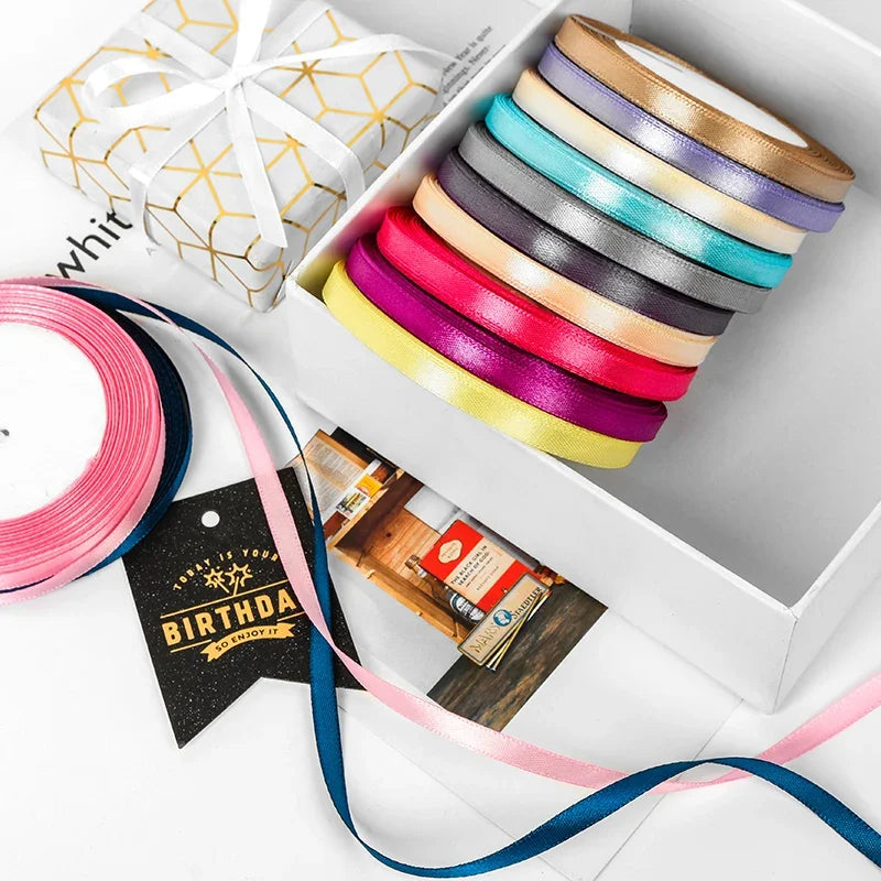 A box filled with various satin ribbon spools in pastel and jewel tones, including pink, purple, blue, and yellow.