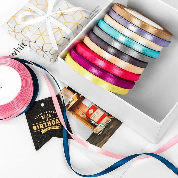 A box filled with various satin ribbon spools in pastel and jewel tones, including pink, purple, blue, and yellow.