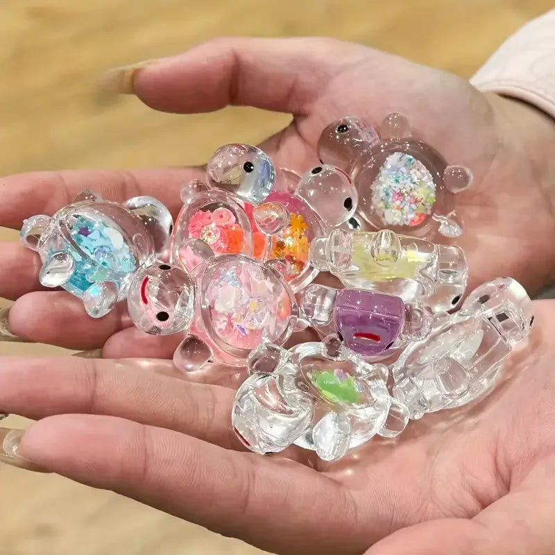 Una mano sostiene una colección de pequeñas estatuas de tortugas marinas de resina translúcida con varios brillos y colores p
