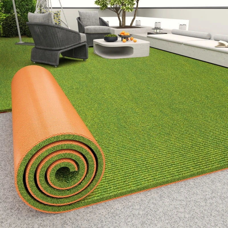 Rolled orange artificial grass carpet lying on a gray floor, with an outdoor living area in the background.