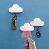 A hand is holding a key attached to a magnetic cloud key hanger against a blue wall.