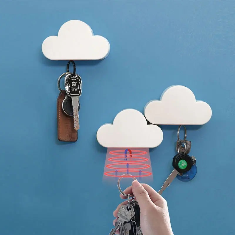 A hand is holding a key attached to a magnetic cloud key hanger against a blue wall.