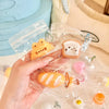 A hand holds several clear plastic pouches containing cute cartoon food squeeze toys and keychains.