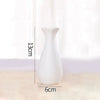 A white ceramic bud vase with a slender neck and rounded body is shown against a light background.