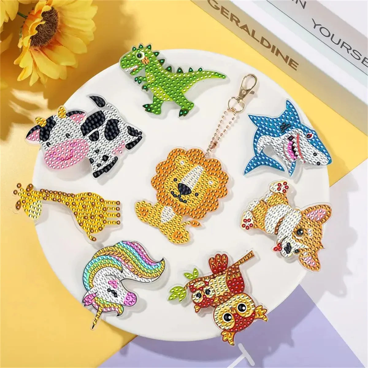 A collection of DIY diamond painting keychains featuring dinosaur, tiger, and animal figures on a white plate.