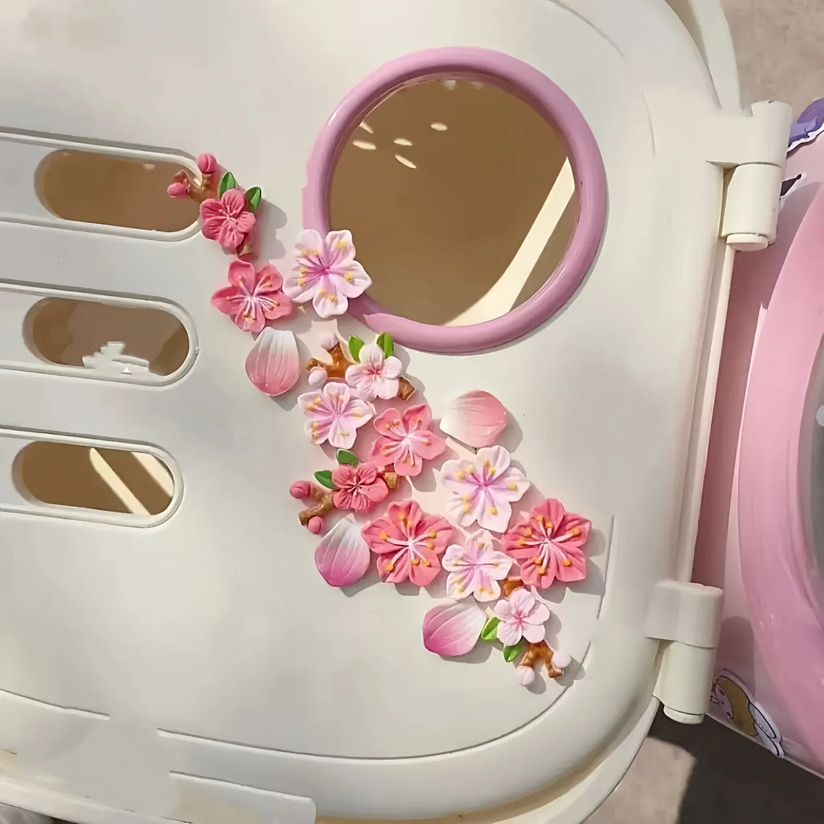 A white car dashboard ornament featuring a pink circular mirror and pink floral decorations.