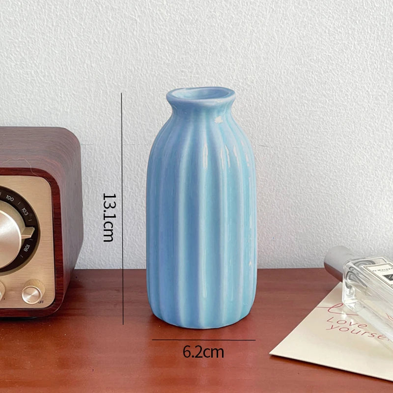 A light blue ceramic bud vase with vertical ridges sitting on a wooden surface.