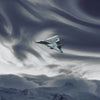 A military jet aircraft flying through swirling clouds above a snowy mountain landscape.