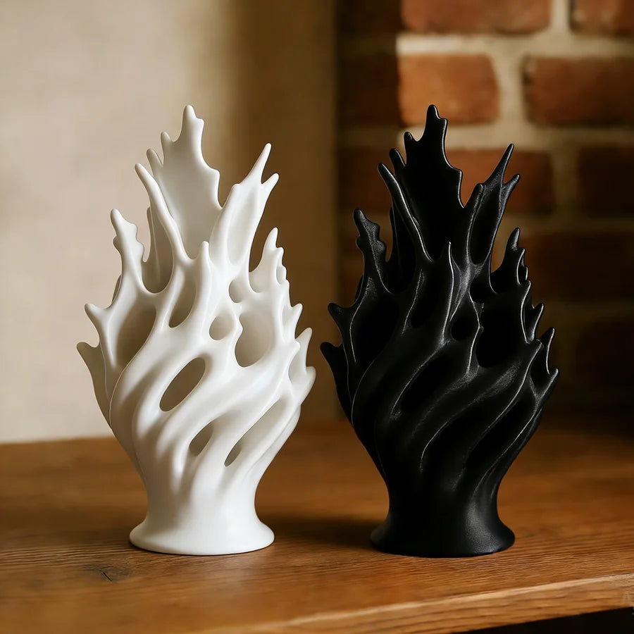 A pair of modern plastic flower vases, one white and one black, displayed on a wooden surface against a brick background.