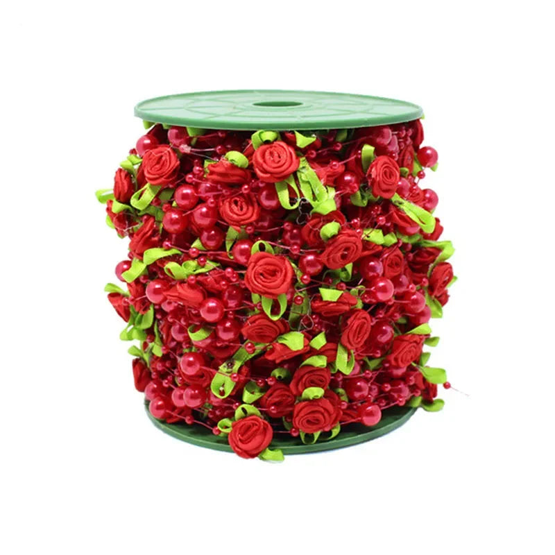 A cylindrical garland made of red roses, pearl beads, and green leaves on a green base.