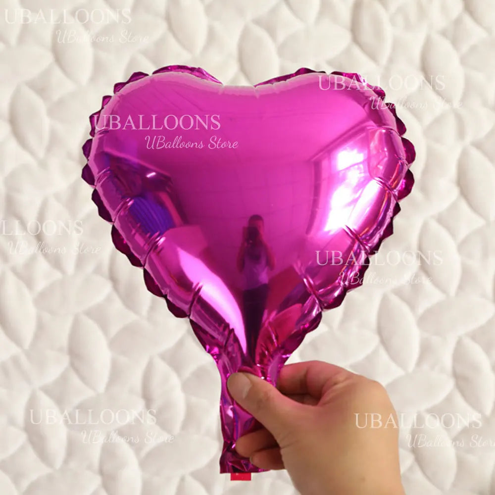 A glossy pink heart-shaped foil balloon being held by a hand against a white quilted background.