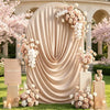 A draped beige fabric arch cover decorated with pink and white floral arrangements for a wedding or event backdrop.