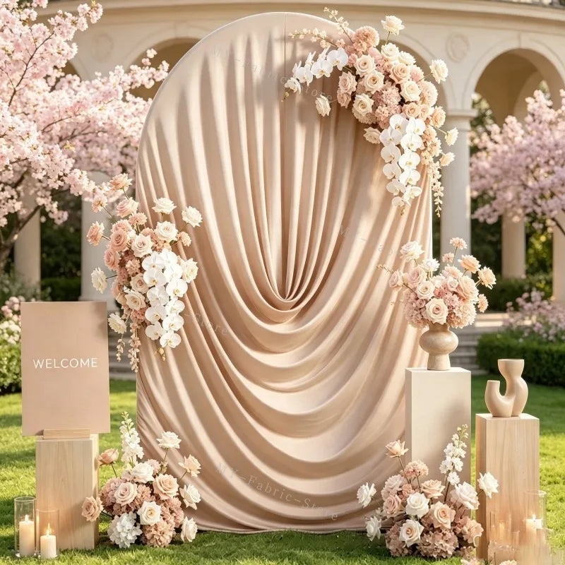 A draped beige fabric arch cover decorated with pink and white floral arrangements for a wedding or event backdrop.