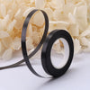 A roll of black satin balloon ribbon is shown against a background of light yellow flowers.