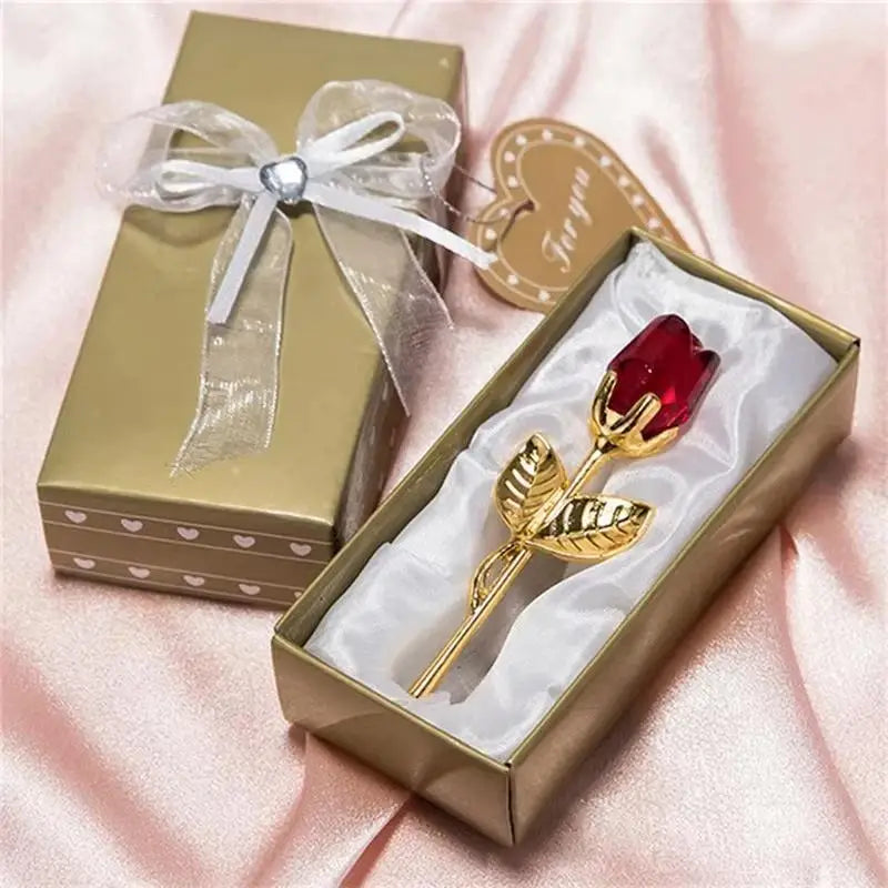 A gold-colored box with a ribbon and an open box containing a crystal red rose artificial flower.