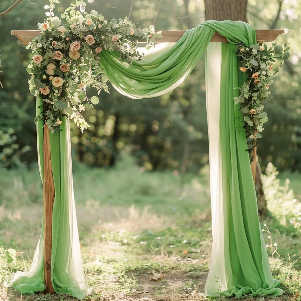 A wooden arch decorated with flowing sage green and white chiffon drapes and floral greenery for a wedding backdrop.