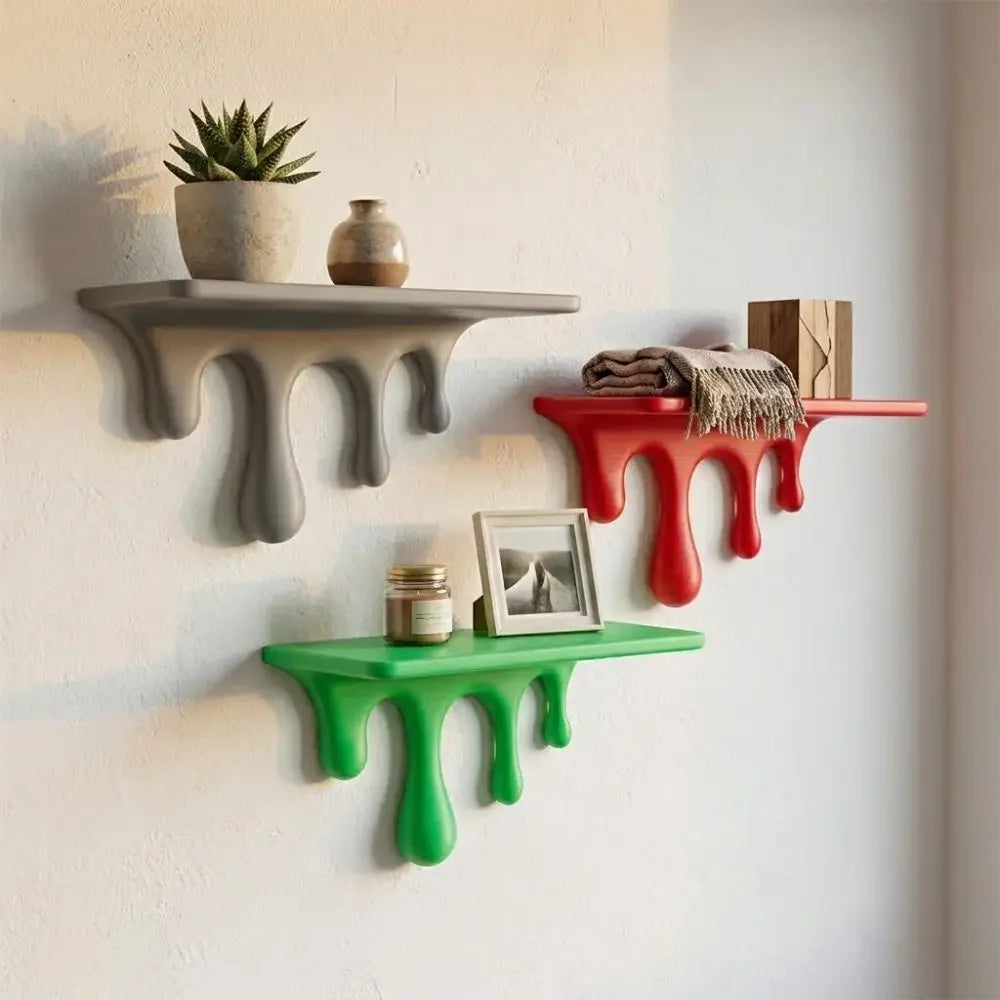 Three drip-style floating shelves in gray, red, and green mounted on a white wall with small potted plants.