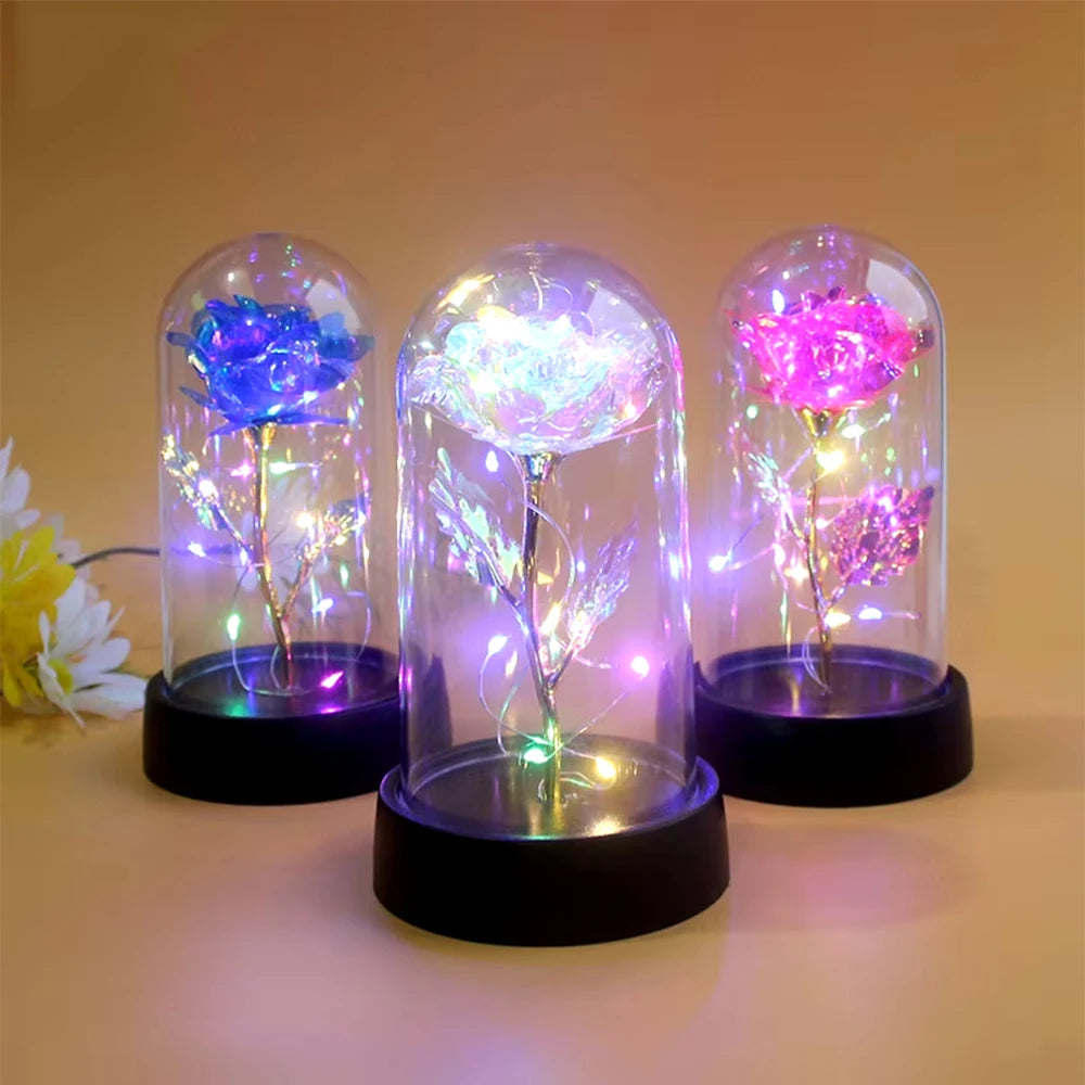 Trois vases en verre en forme de roses avec des lumières LED lumineuses exposés sur une surface.
