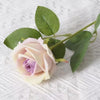 A soft pink and purple artificial rose with green leaves on a stem.