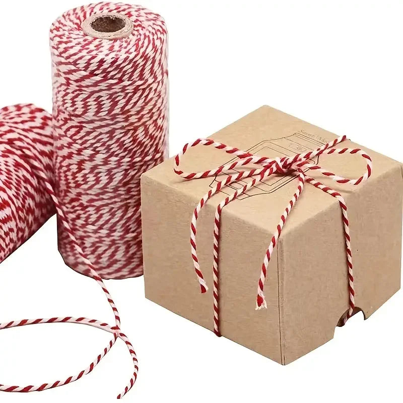 A roll of red and white striped cotton baker's twine next to a cardboard gift box tied with the same twine.