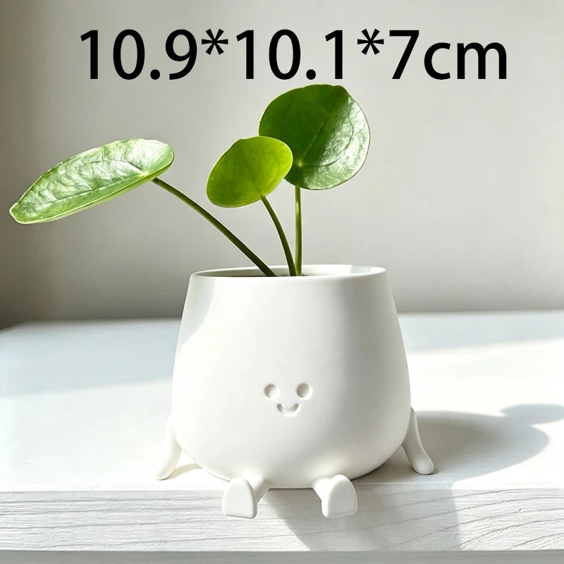 A white 3D printed smiley face succulent planter with green leaves on a light surface.