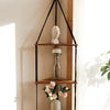 Étagère flottante en bois bohème avec porte-manteau noir pour une buste blanche et des arrangements floraux.