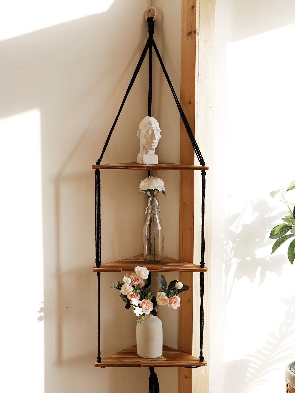 Étagère flottante en bois bohème avec porte-manteau noir pour une buste blanche et des arrangements floraux.
