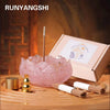 A pink crystal dropper candle set with a wooden stick and incense sticks displayed on a wooden surface.