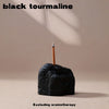 A black tourmaline crystal is shown resting on a surface with a thin stick extending upwards.