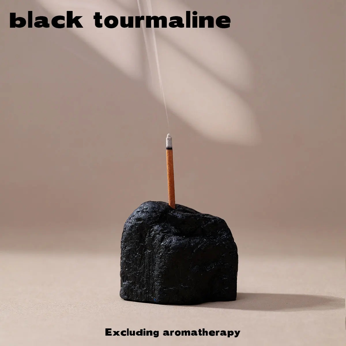 A black tourmaline crystal is shown resting on a surface with a thin stick extending upwards.