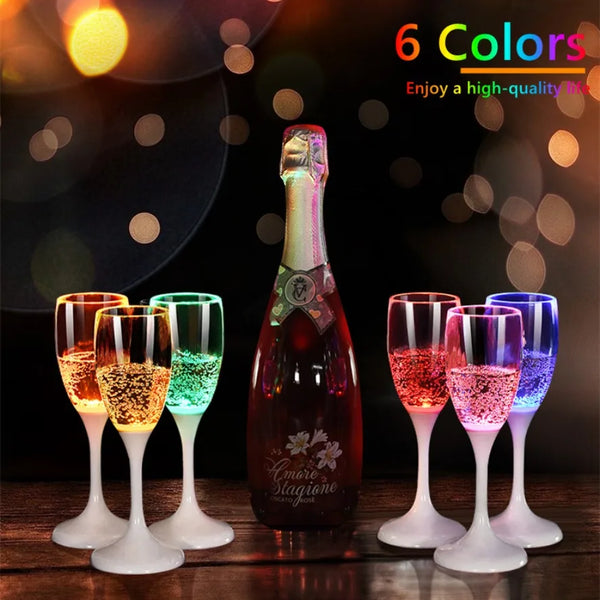 Six multi-color LED flashing drinking glasses displayed on a wooden surface with a bottle in the background.
