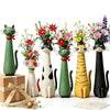 A collection of whimsical resin cat-shaped flower vases in various shades of green, black, and yellow.