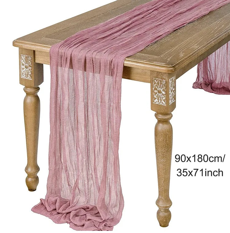 A long, sheer mauve gauze fabric draped over a wooden table.
