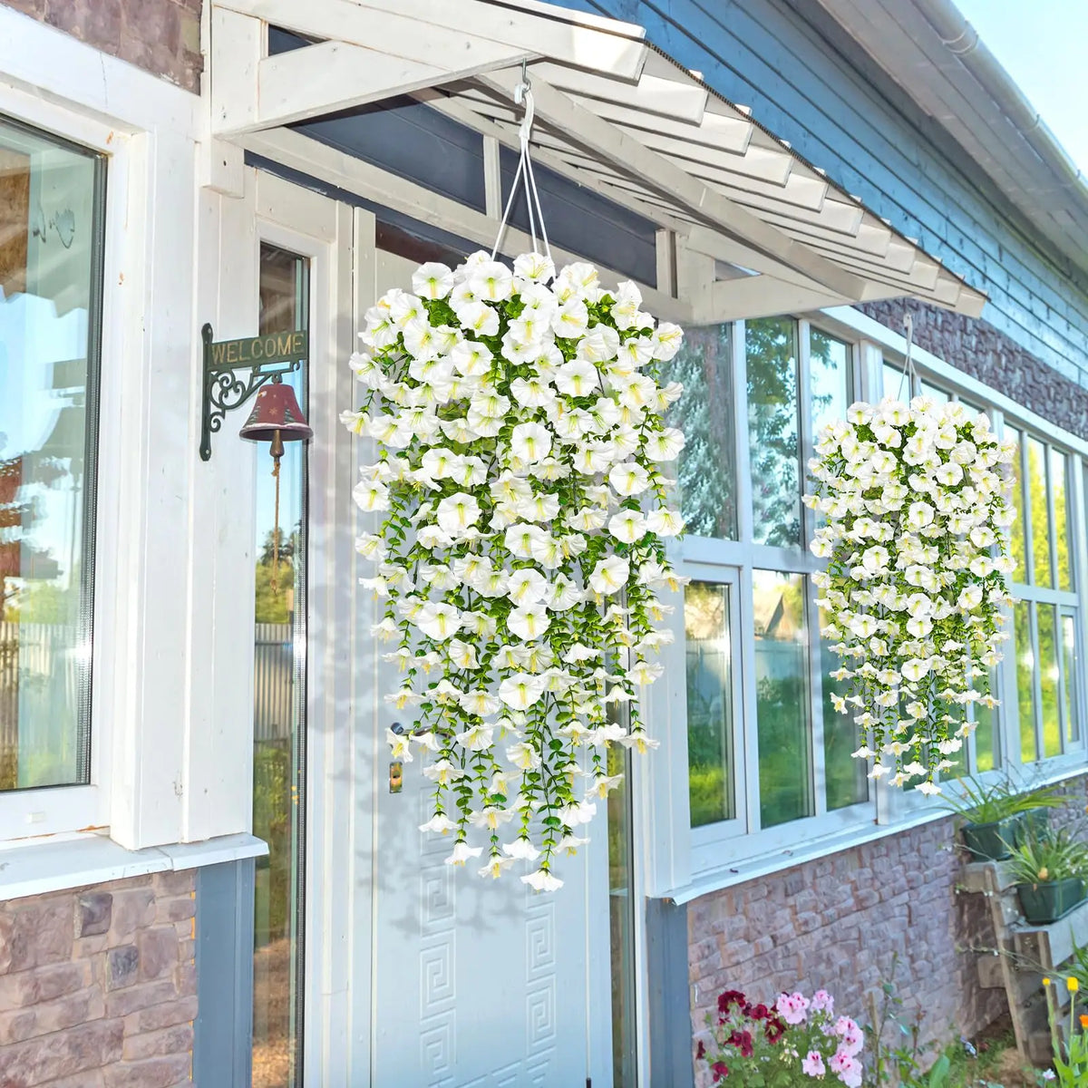 A white artificial morning glory plant hangs in a basket on the door of a house.
