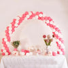 A pink and white balloon arch decoration on a table with floral arrangements.