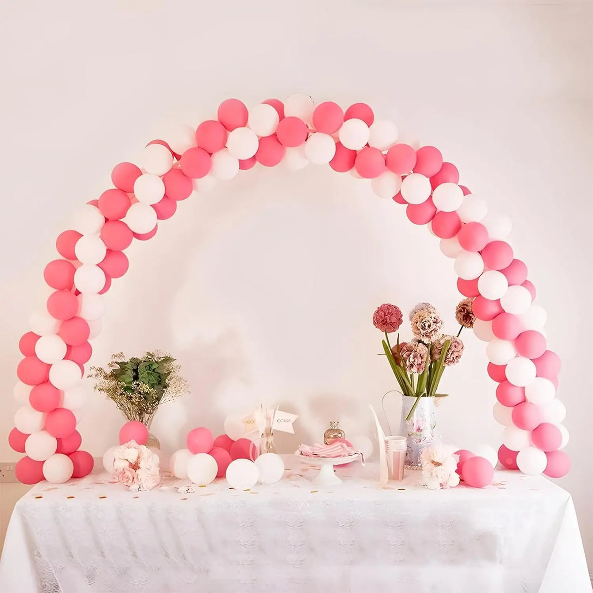 A pink and white balloon arch decoration on a table with floral arrangements.