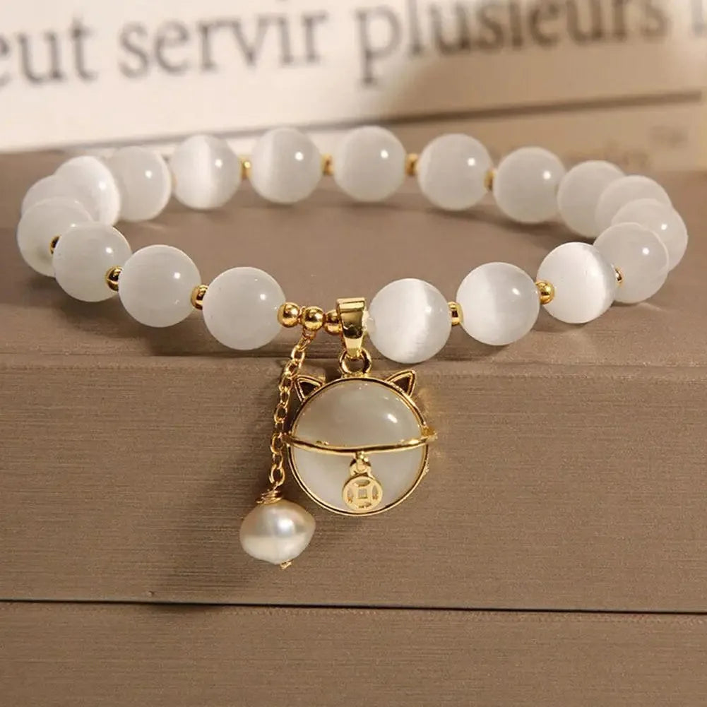 A bracelet made of small, round white natural stones with a gold-toned charm and pearl drop on a wooden surface.