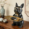 A black decorative bulldog figurine wearing gold sunglasses and holding a leather key on a gold tray.